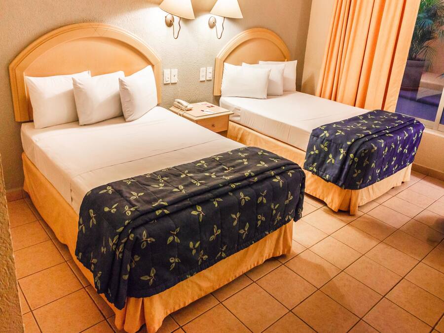 A hotel room with two beds, a nightstand, and a lamp.