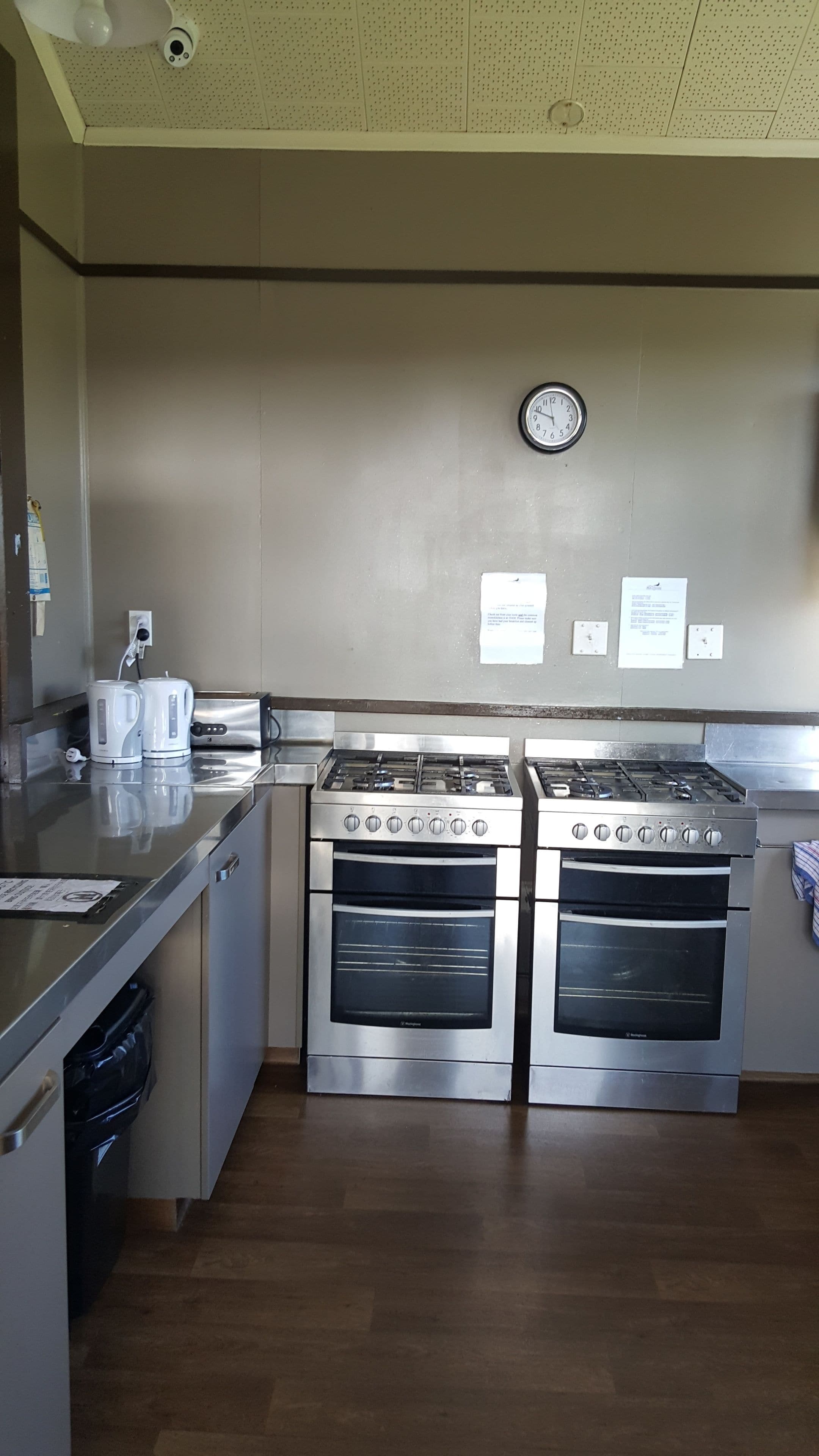 A kitchen with two stainless steel ovens, a clock on the wall, and a coffee maker on the counter.