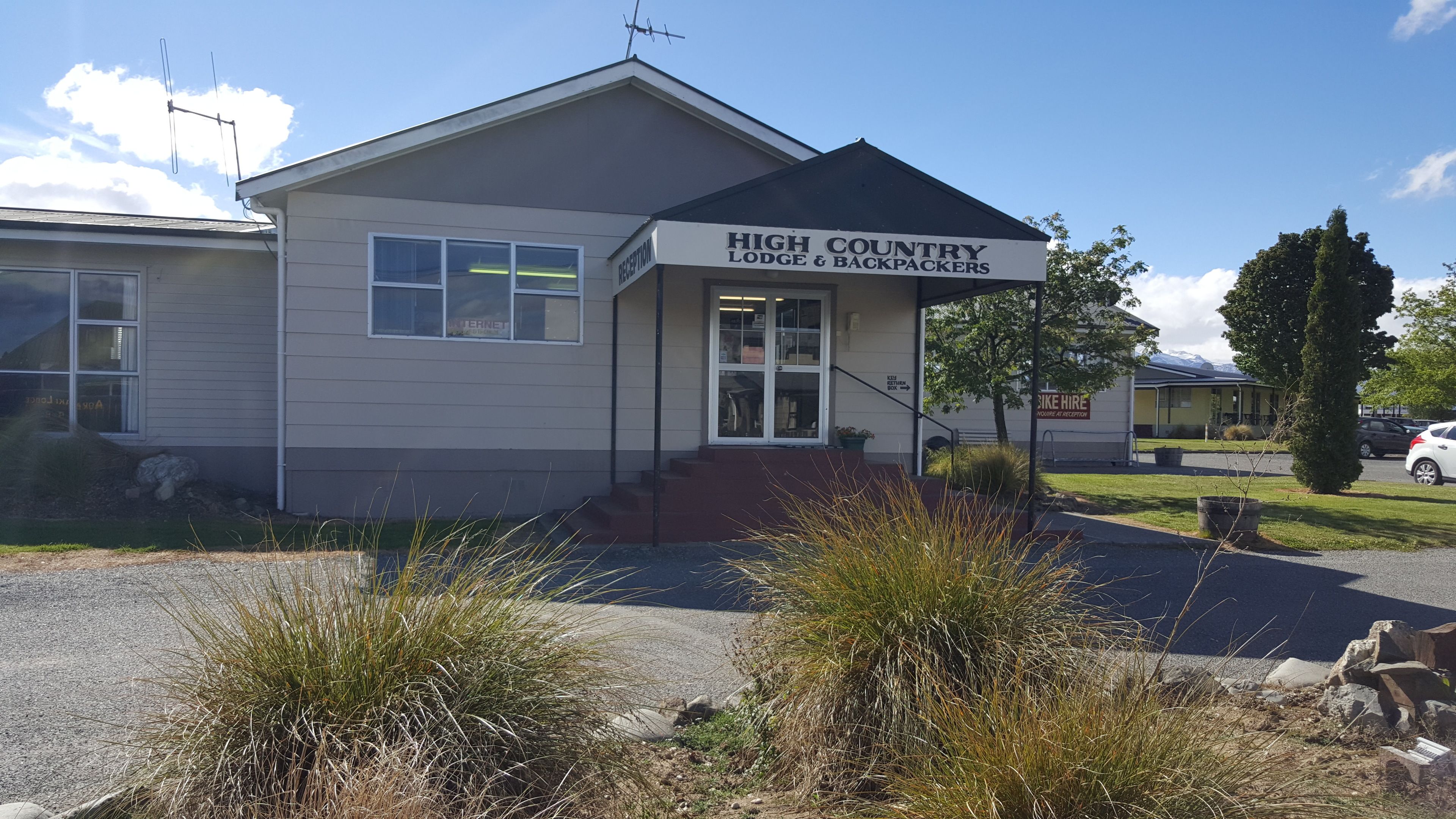A building labeled "High Country Lodge & Backpackers" with a reception area, steps leading to the entrance, and a sign for bike hire.