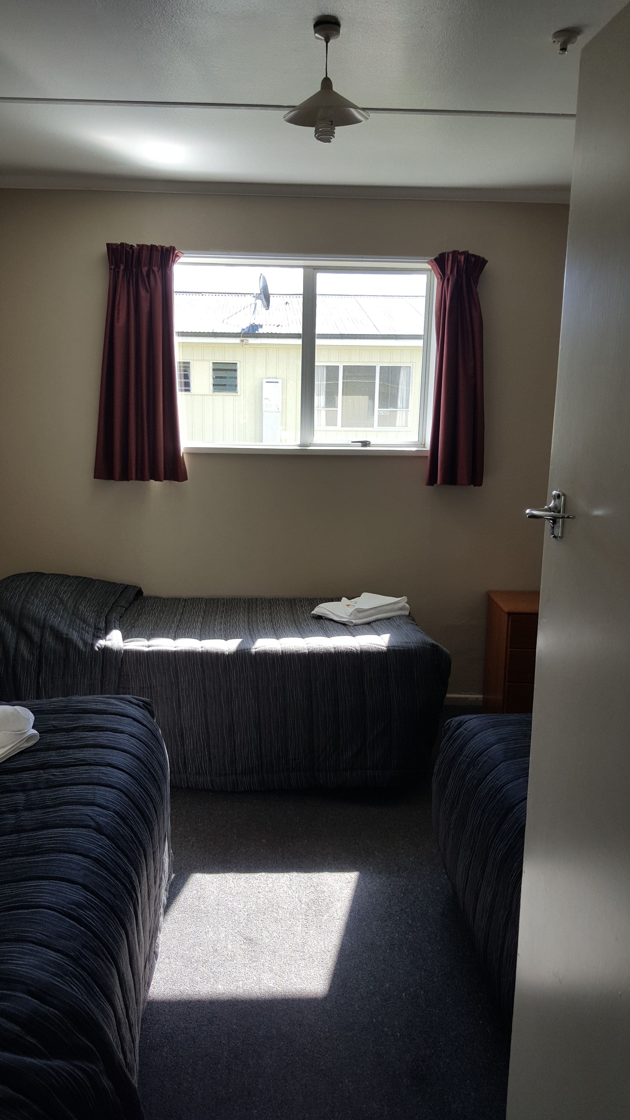 Ein Zimmer mit zwei Einzelbetten, einem Deckenventilator, einem Fenster mit Vorhängen und einer Tür.