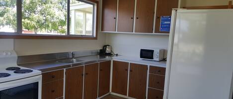 A kitchen with wooden cabinets, a white stove, a microwave, and a refrigerator.