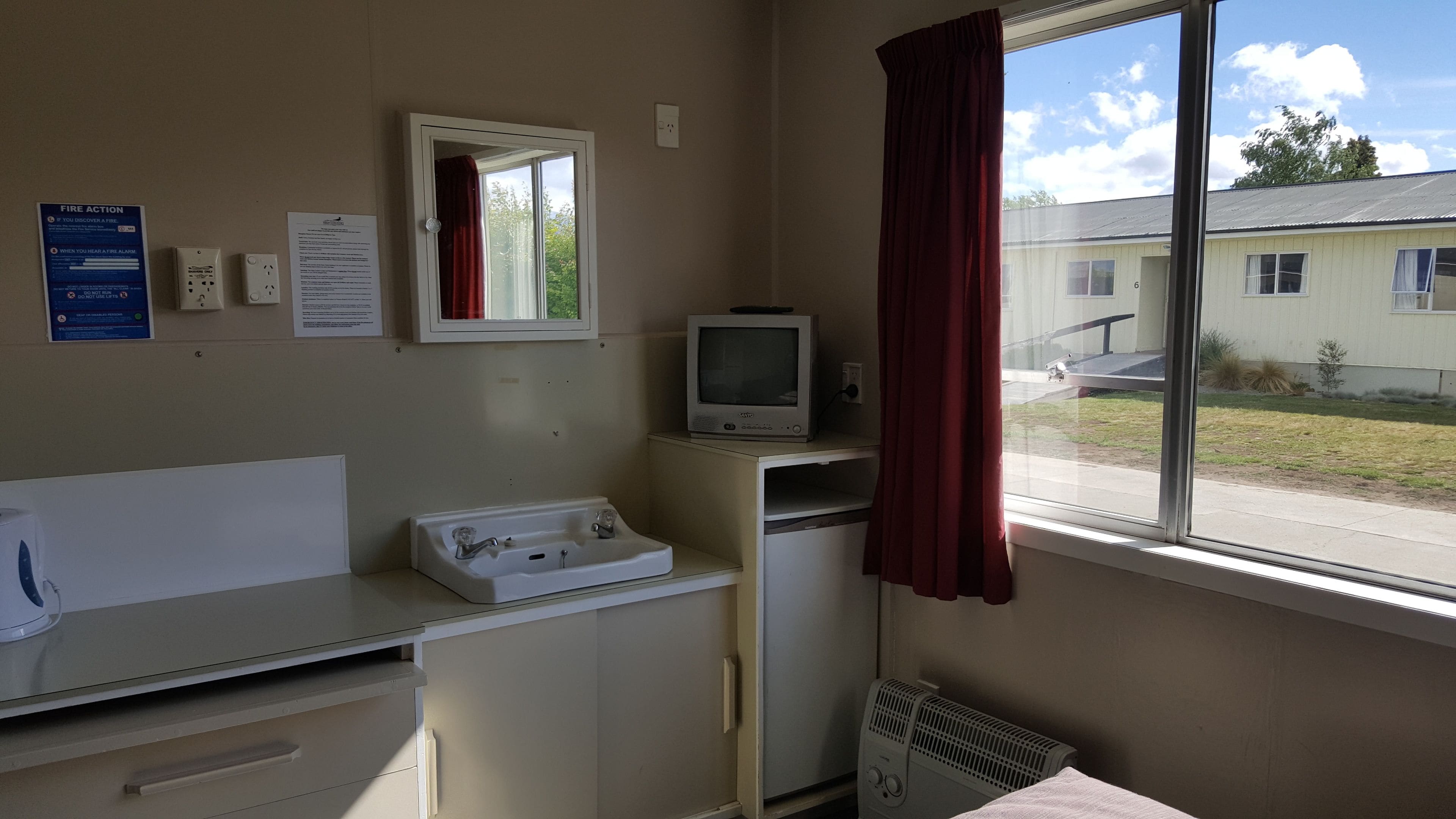 Una habitación pequeña y sencilla, con un lavabo, un espejo y un televisor sobre un mueble.