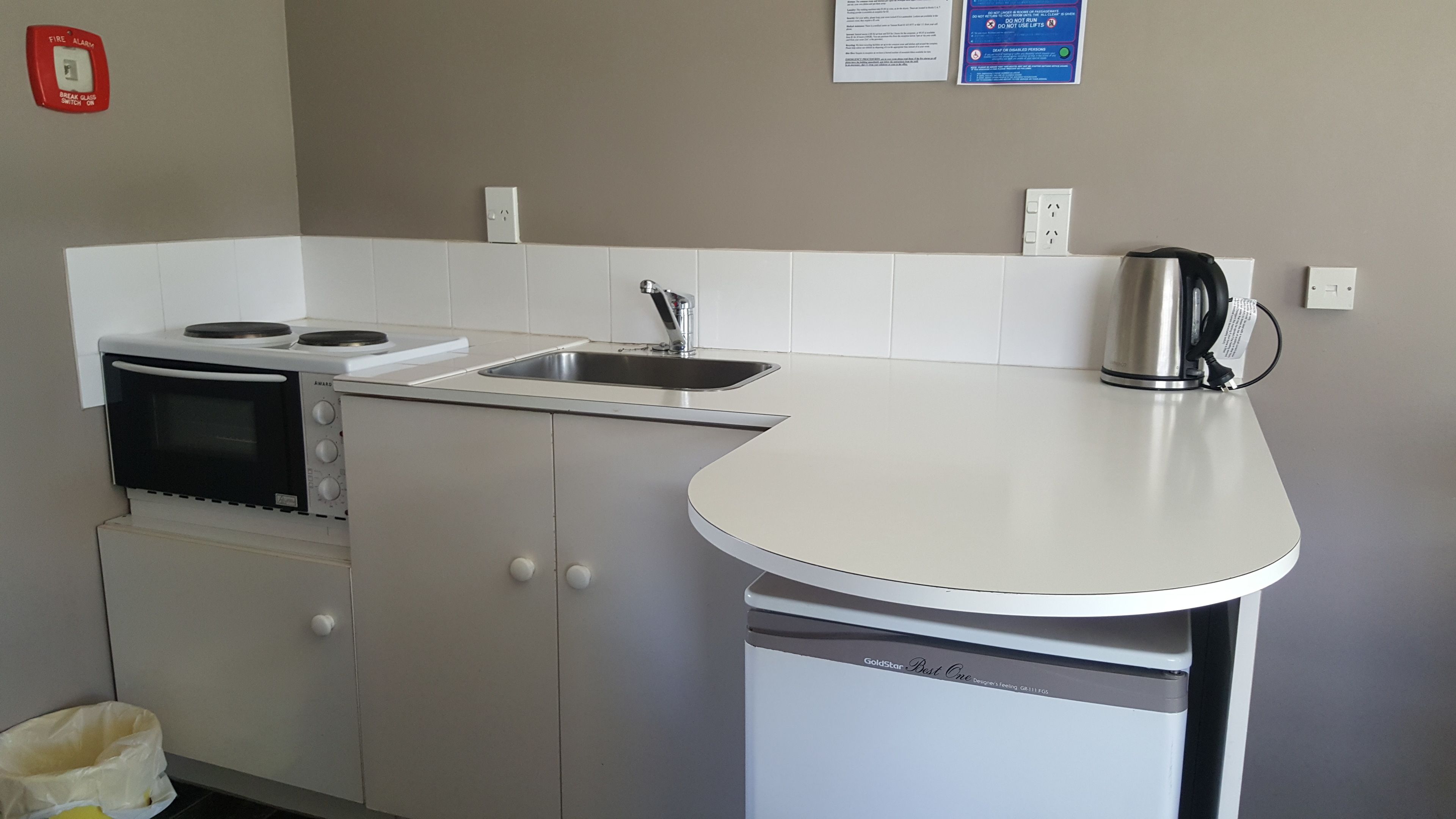 A compact kitchenette with a stove, oven, sink, and a coffee maker.