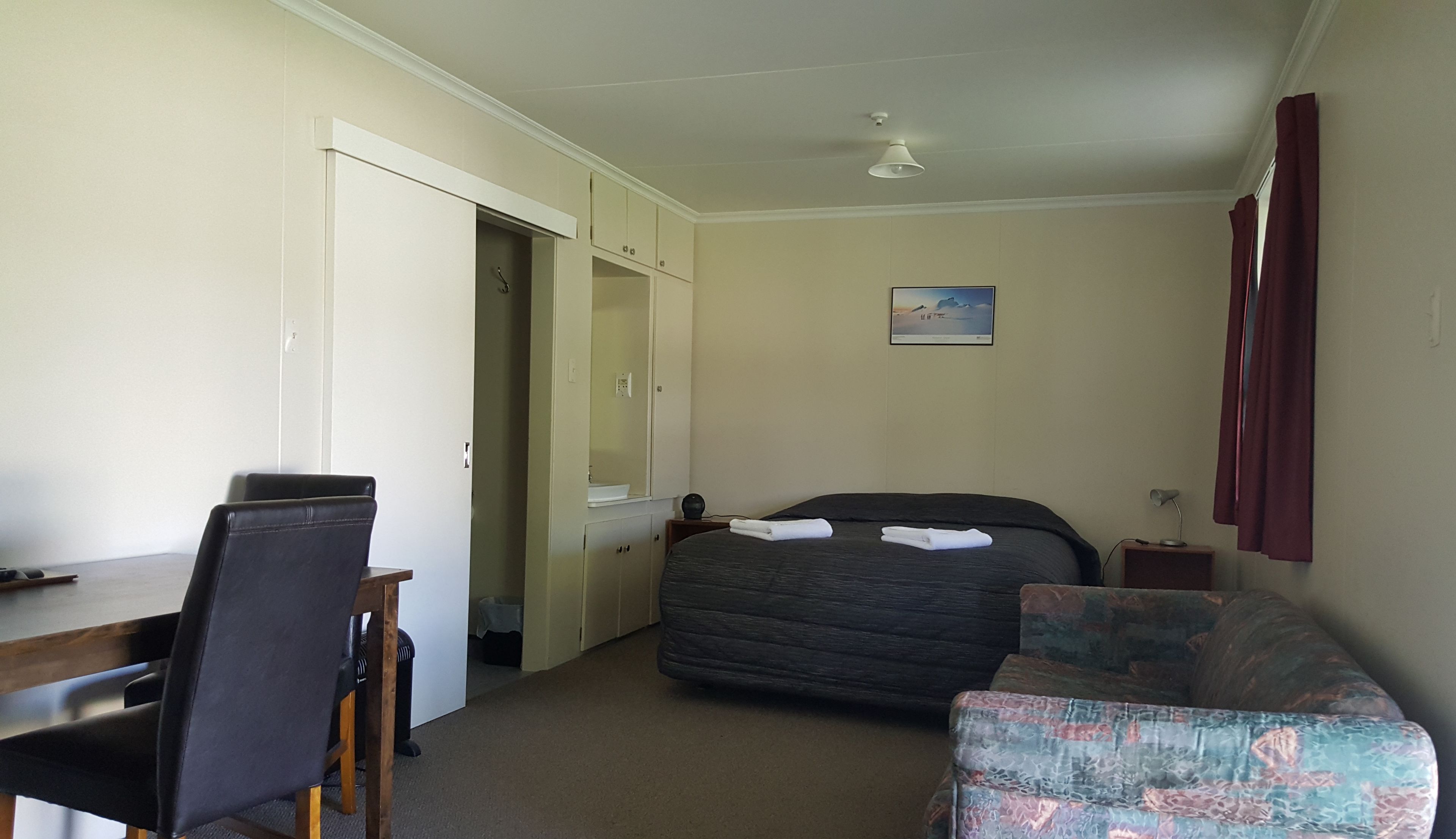A hotel room with a bed, a desk, a chair, a small table, and a nightstand.