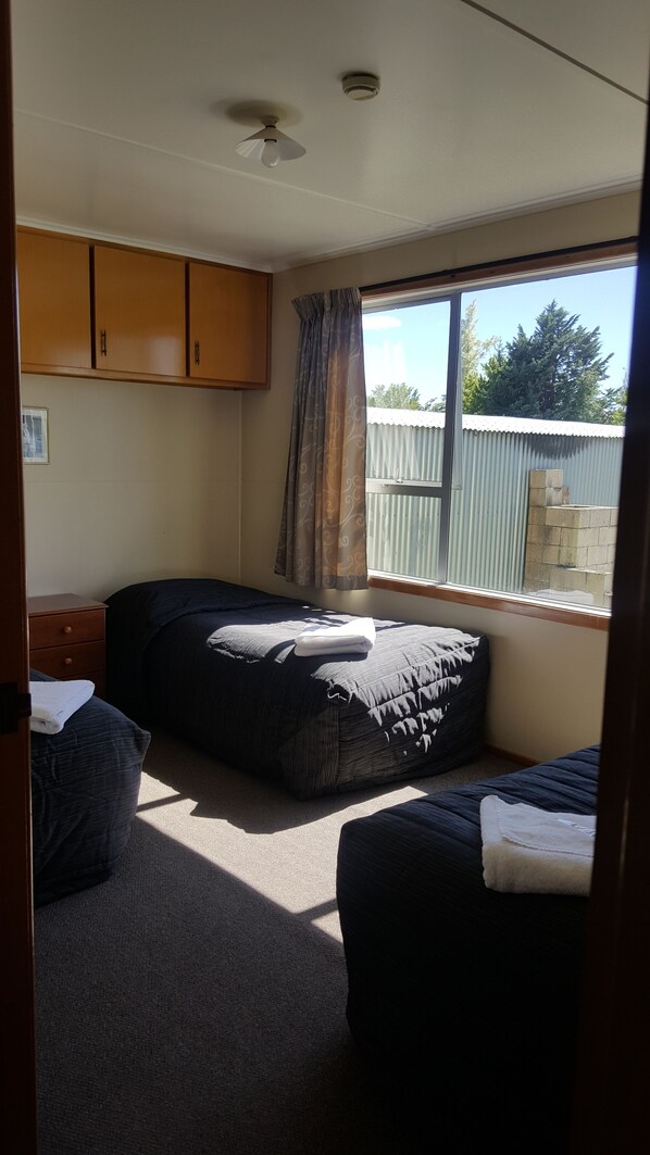 A bedroom with two beds, a ceiling fan, a window with curtains, and wooden cabinets.