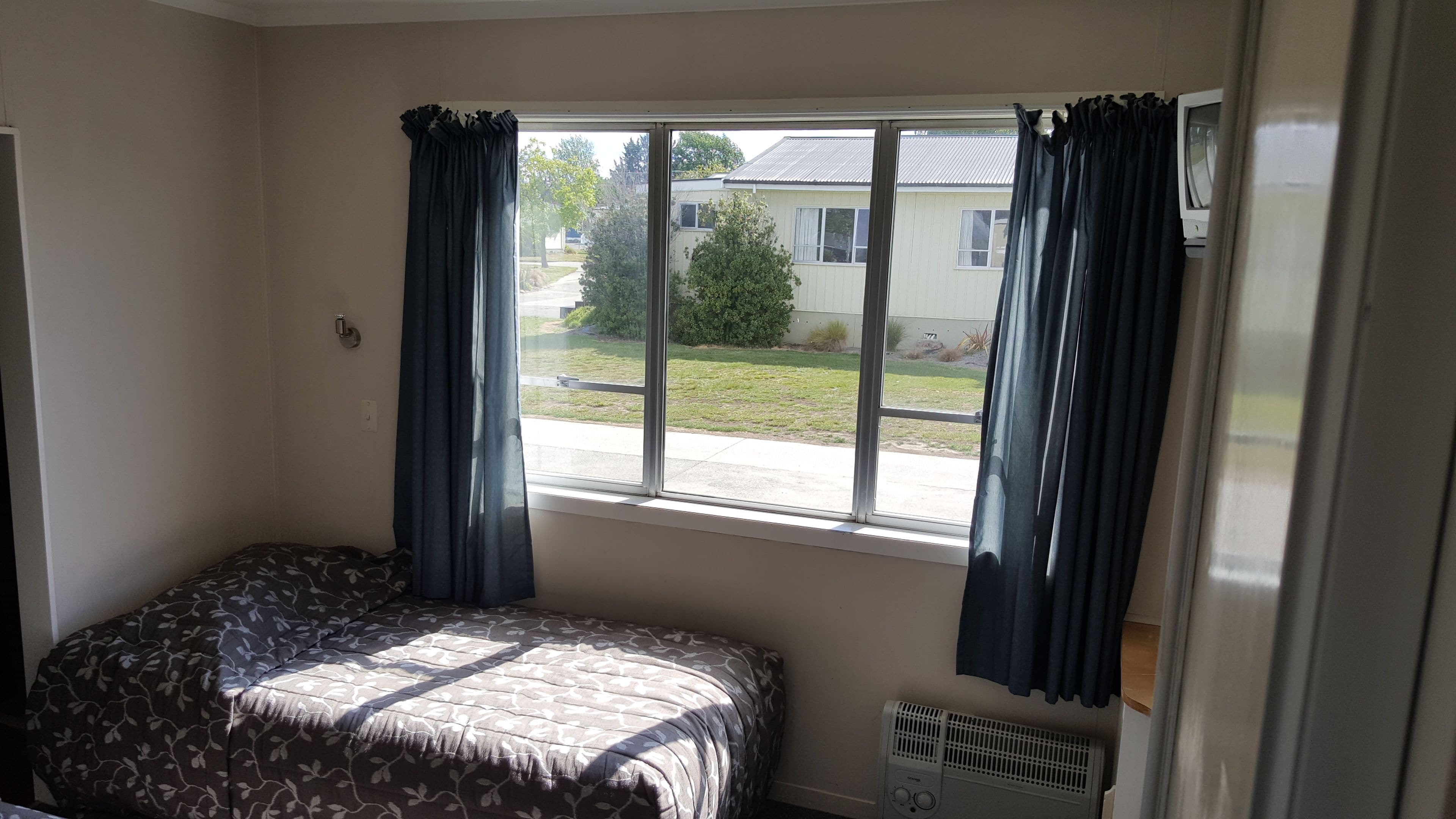 A bedroom with a single bed, a window with curtains, and a radiator.