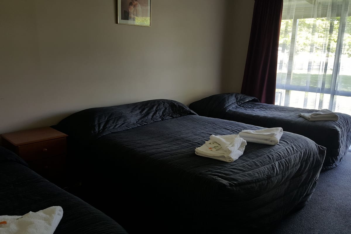 Ein Hotelzimmer mit zwei Betten, einem Nachttisch und einem Fenster mit Vorhängen.