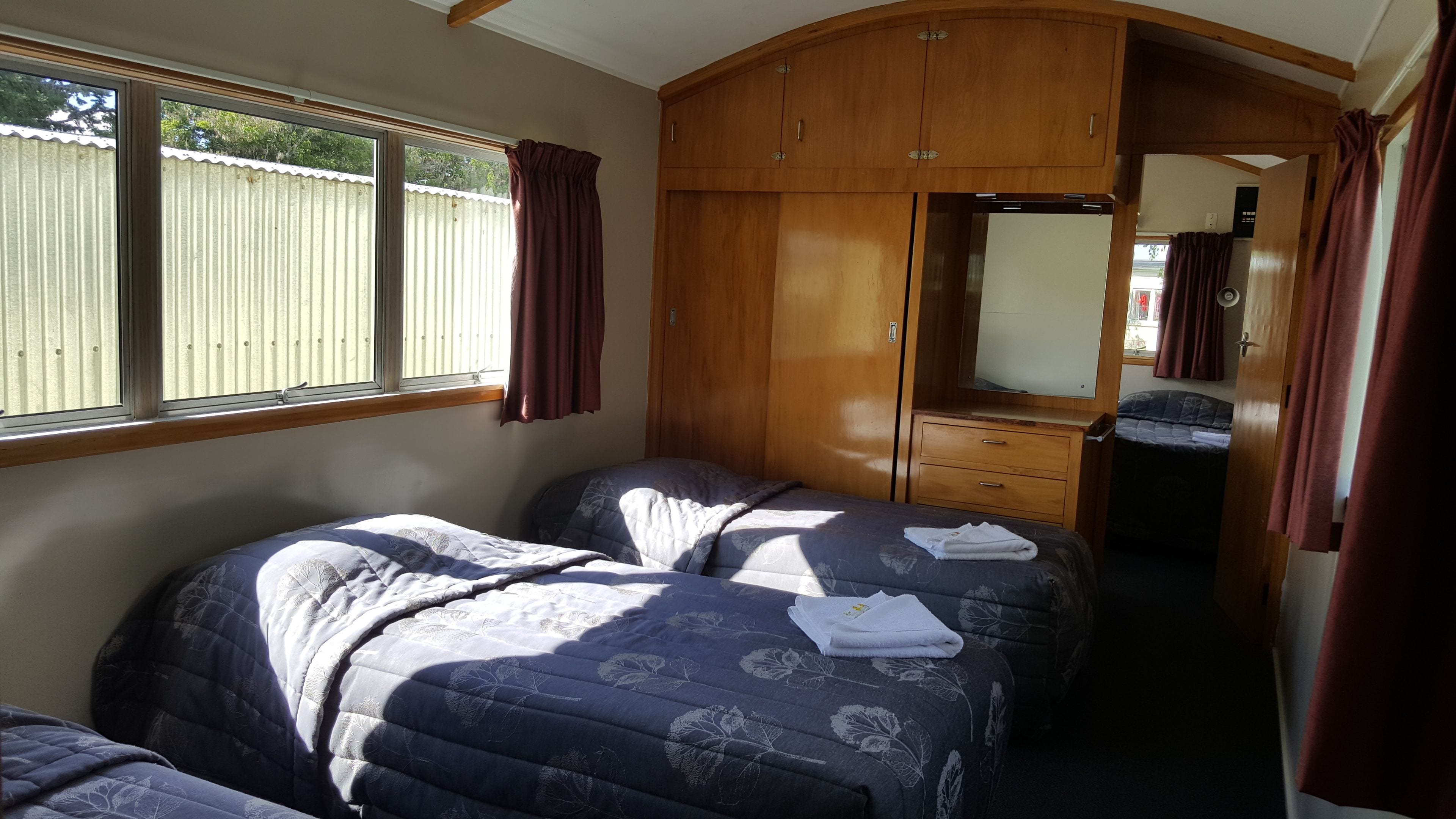 Une chambre avec deux lits, une armoire en bois et un miroir.