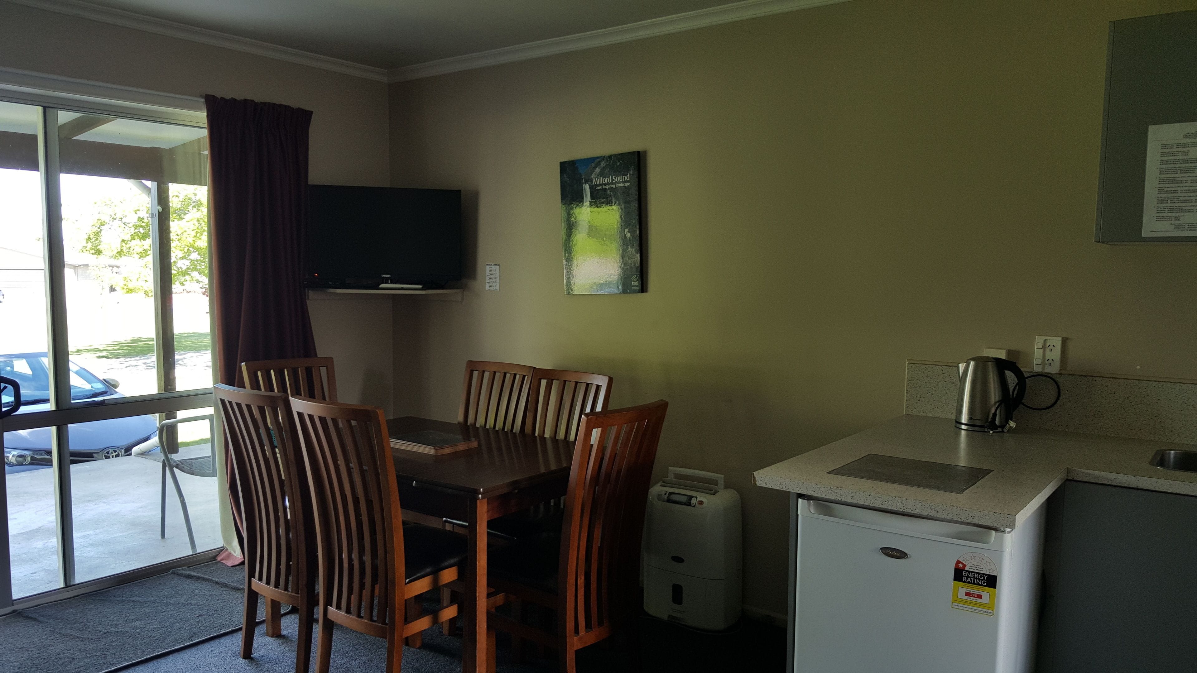 Une cuisine compacte comprenant une table à manger, des chaises, un petit réfrigérateur, une machine à café et un téléviseur fixé au mur.