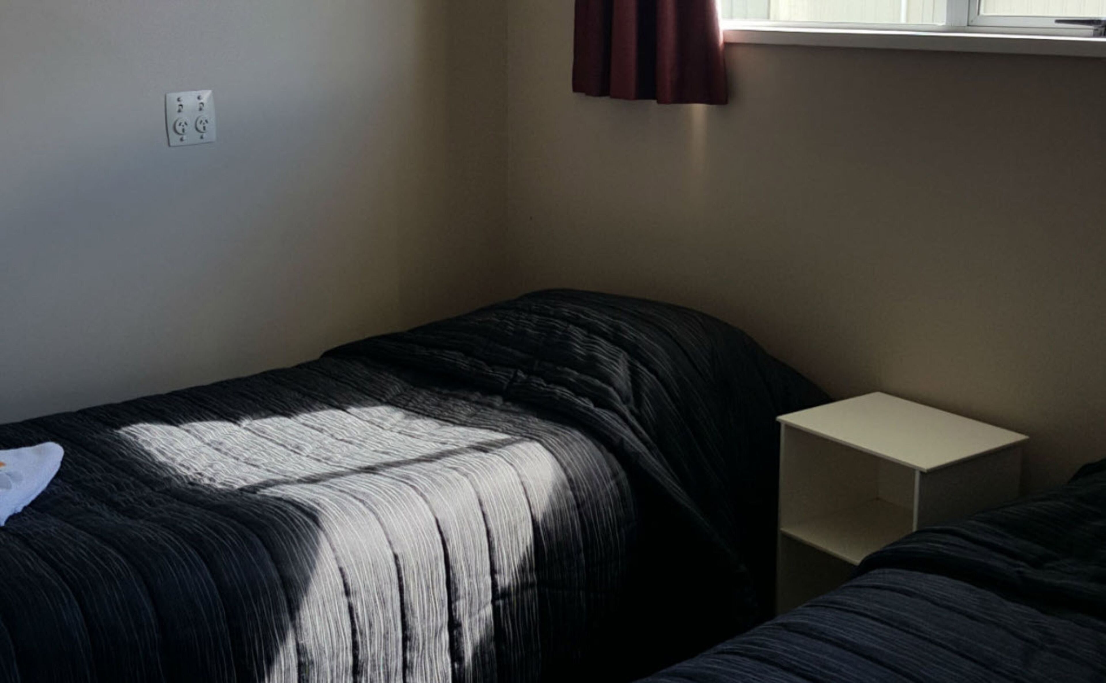 A single bed with a black and white striped blanket, a white bedside table, and a window with curtains.