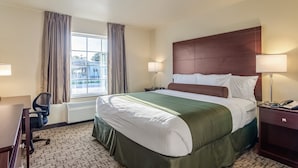 Ein Hotelzimmer mit einem großen Bett, zwei Nachttischlampen, einem Schreibtisch mit Stuhl und einem Fenster mit Vorhängen.