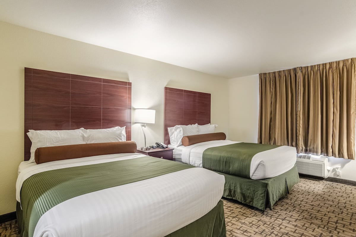 A hotel room with two beds, a nightstand, a lamp, and a window with curtains.
