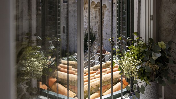 A view through a window with a metal grill, featuring terracotta steps and a brick wall in the background.