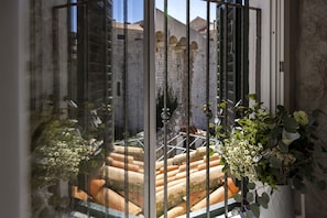 Vista a través de una ventana con una reja de metal, que muestra escalones de terracota y un muro de ladrillo al fondo.