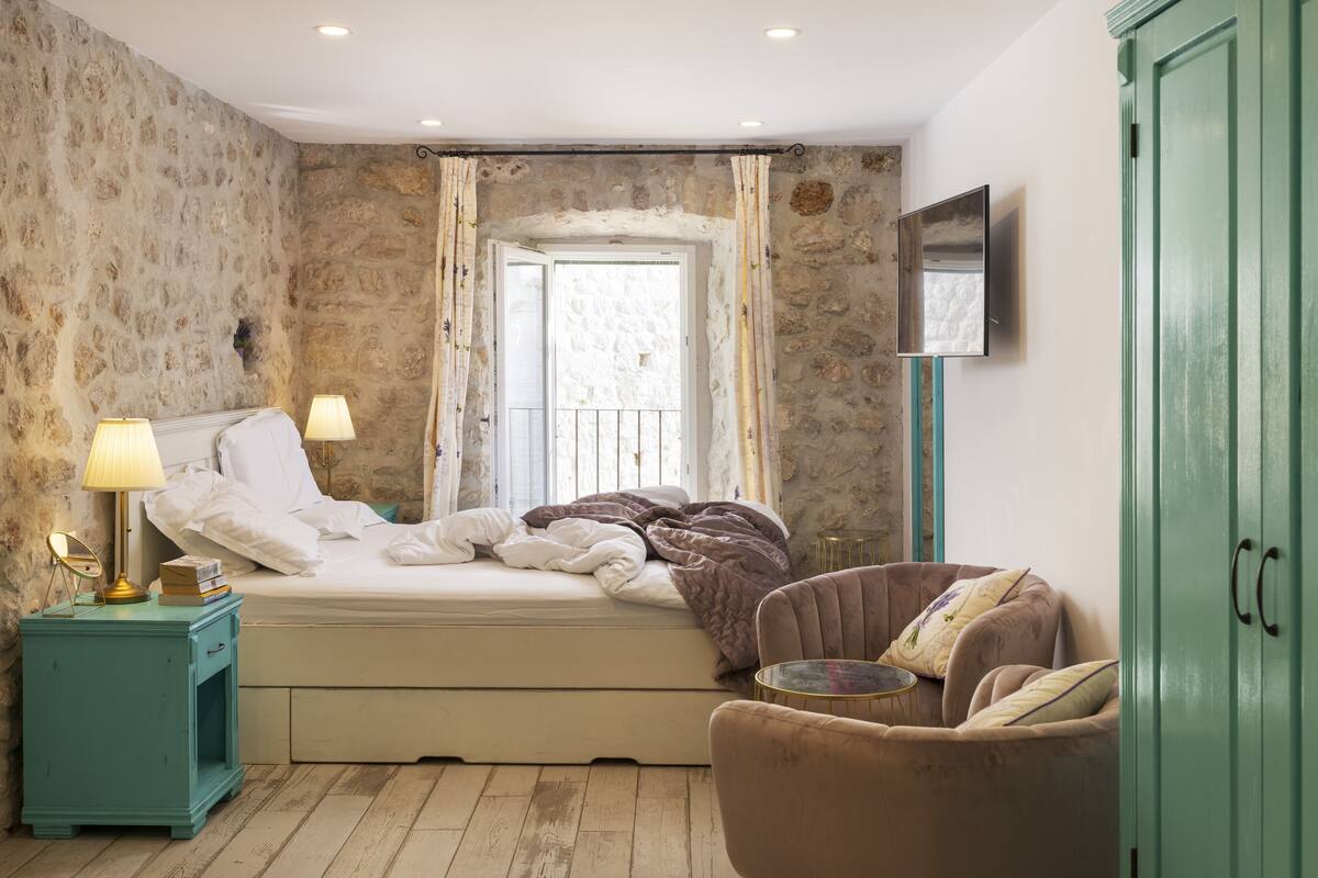 A bedroom with a bed, a nightstand, a chair, a wardrobe, and a window with curtains.