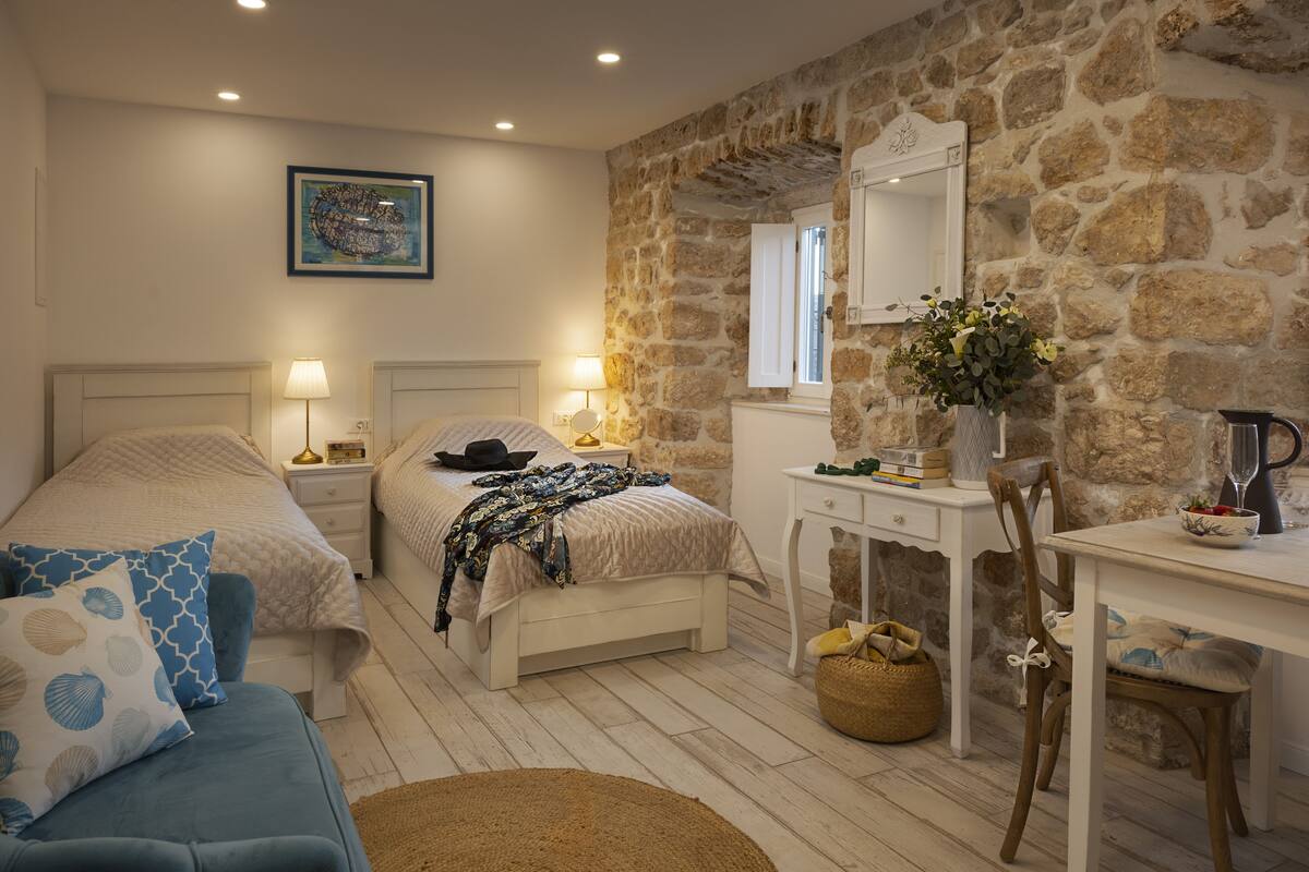 A bedroom with two beds, a desk, and a stone wall.