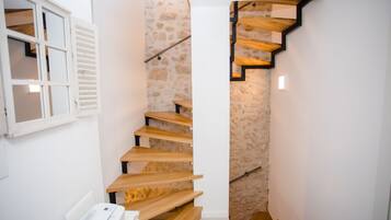 Una escalera con peldaños de madera y un muro de piedra que conduce a una habitación con una puerta blanca y una ventana con contraventanas.