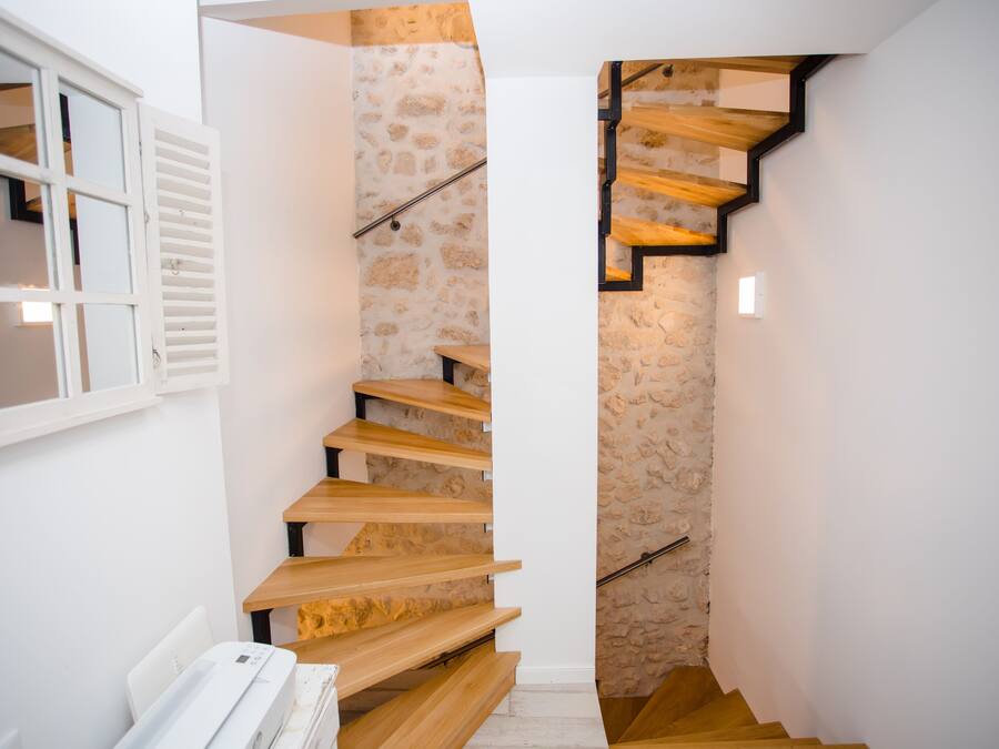 Una escalera con peldaños de madera y un muro de piedra que conduce a una habitación con una puerta blanca y una ventana con contraventanas.