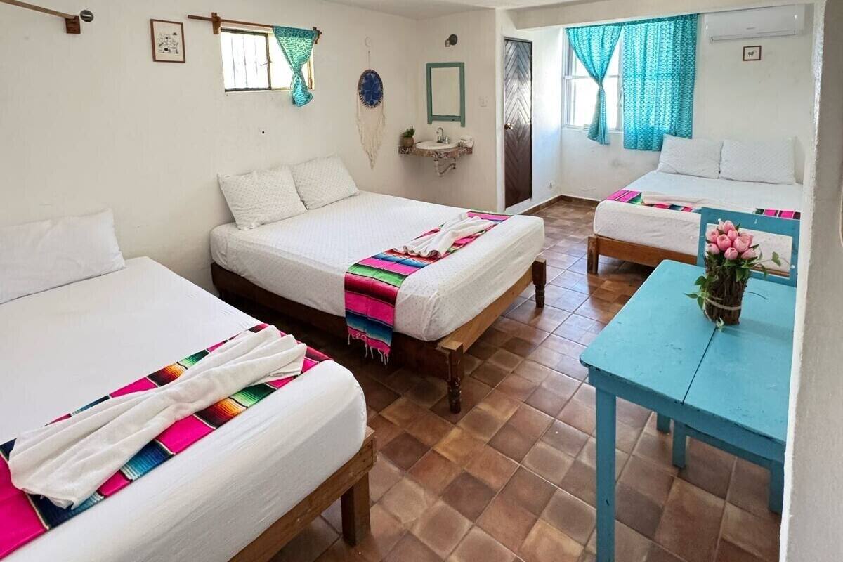 A room with two beds, a small table with a vase of flowers, and a window with curtains.