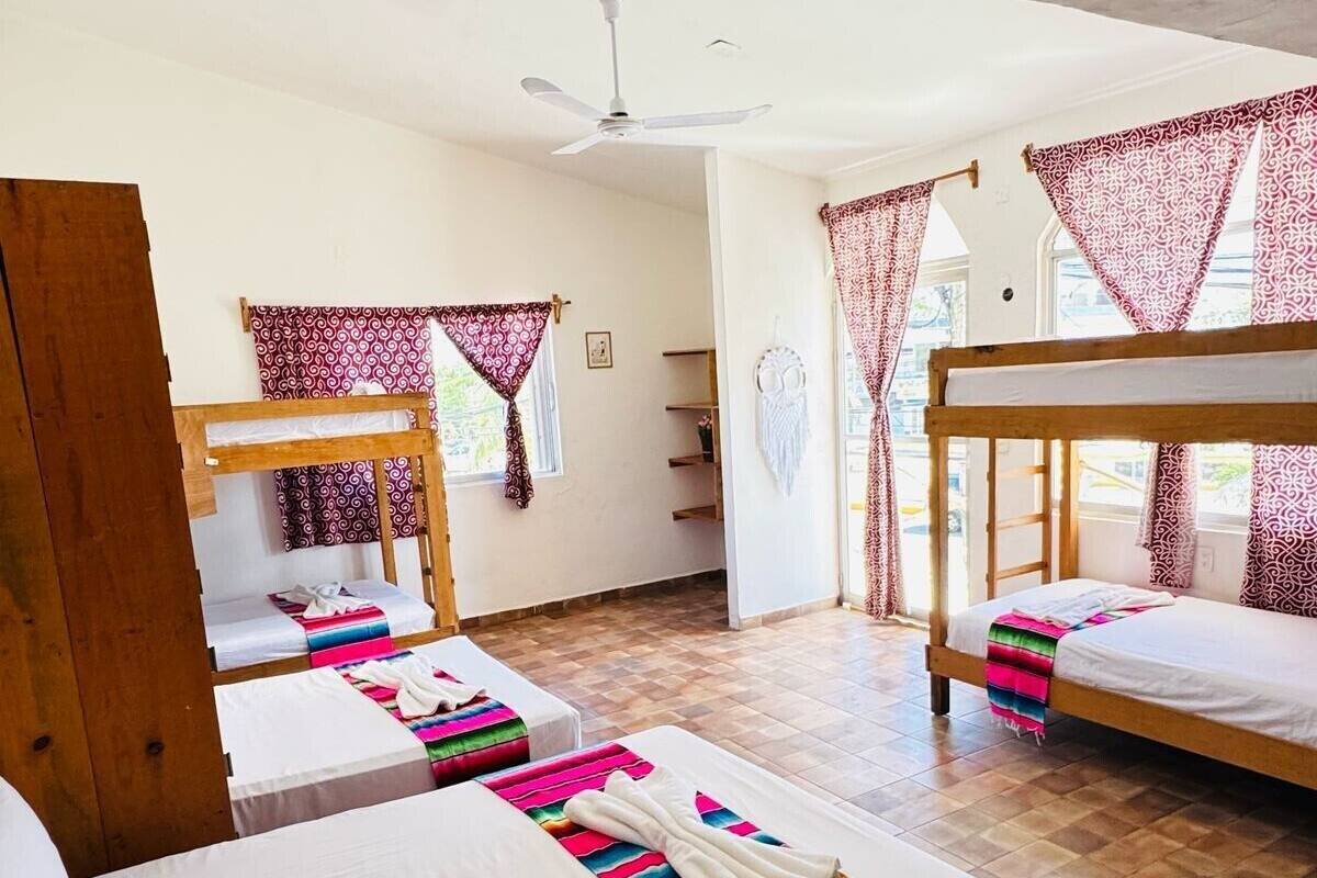 A hotel room with two single beds, a wooden bunk bed, a ceiling fan, and patterned curtains.