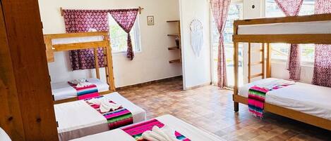 A hotel room with two single beds, a wooden bunk bed, a ceiling fan, and patterned curtains.