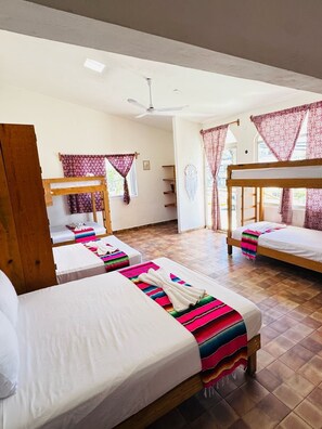A hotel room with two single beds, a wooden bunk bed, a ceiling fan, and patterned curtains. - Naay Bej (Tulum)