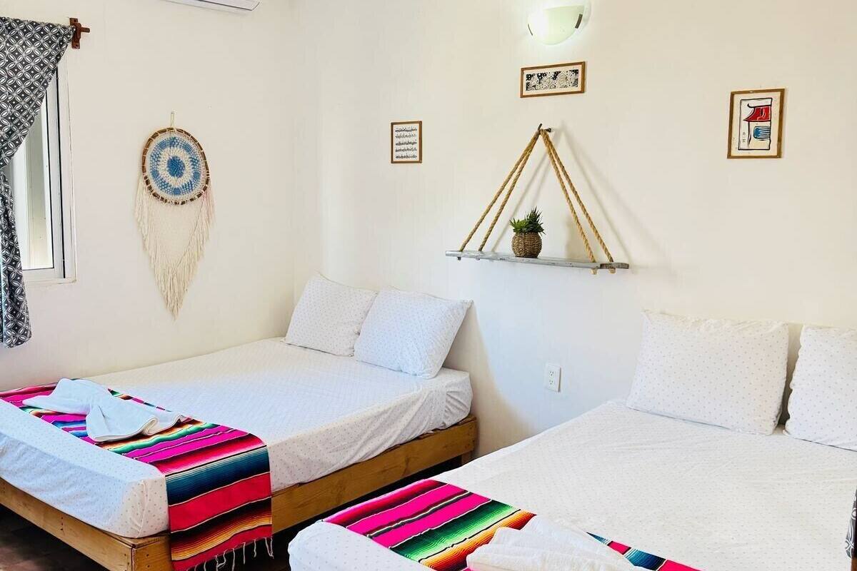 A room with two beds, a ceiling fan, a wall-mounted air conditioner, and a small shelf with a plant.