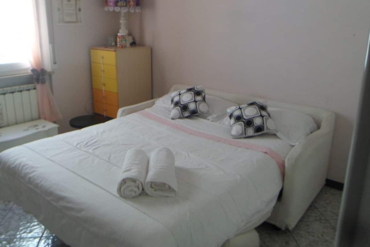 Un lit bien fait, avec une couette blanche et deux oreillers, une petite table de chevet avec une lampe, et une armoire jaune dans une chambre.