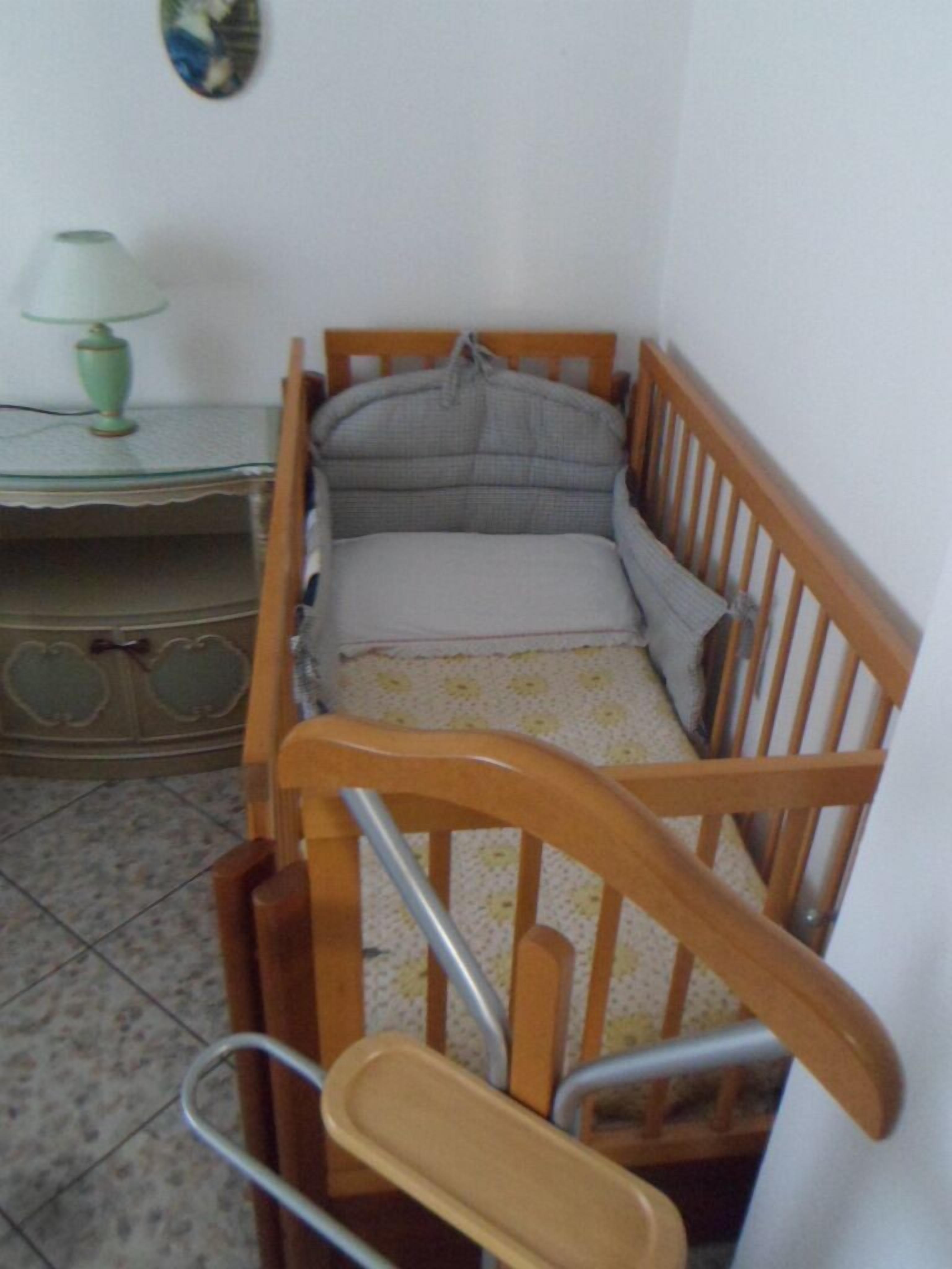 A small, cozy room with a wooden crib, a small table with a lamp, and a patterned rug.