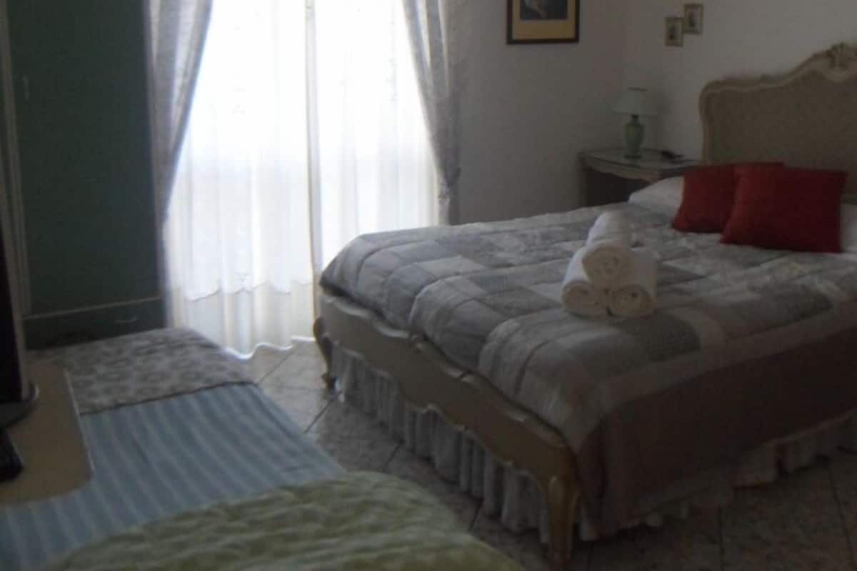 Une chambre à coucher avec un lit, une table de chevet, une lampe et une fenêtre avec des rideaux.