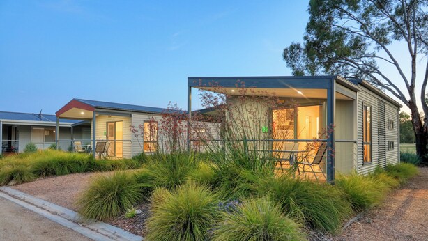 Un bâtiment moderne, de plain-pied, doté d’un espace extérieur couvert avec des sièges et d’un jardin bien entretenu.