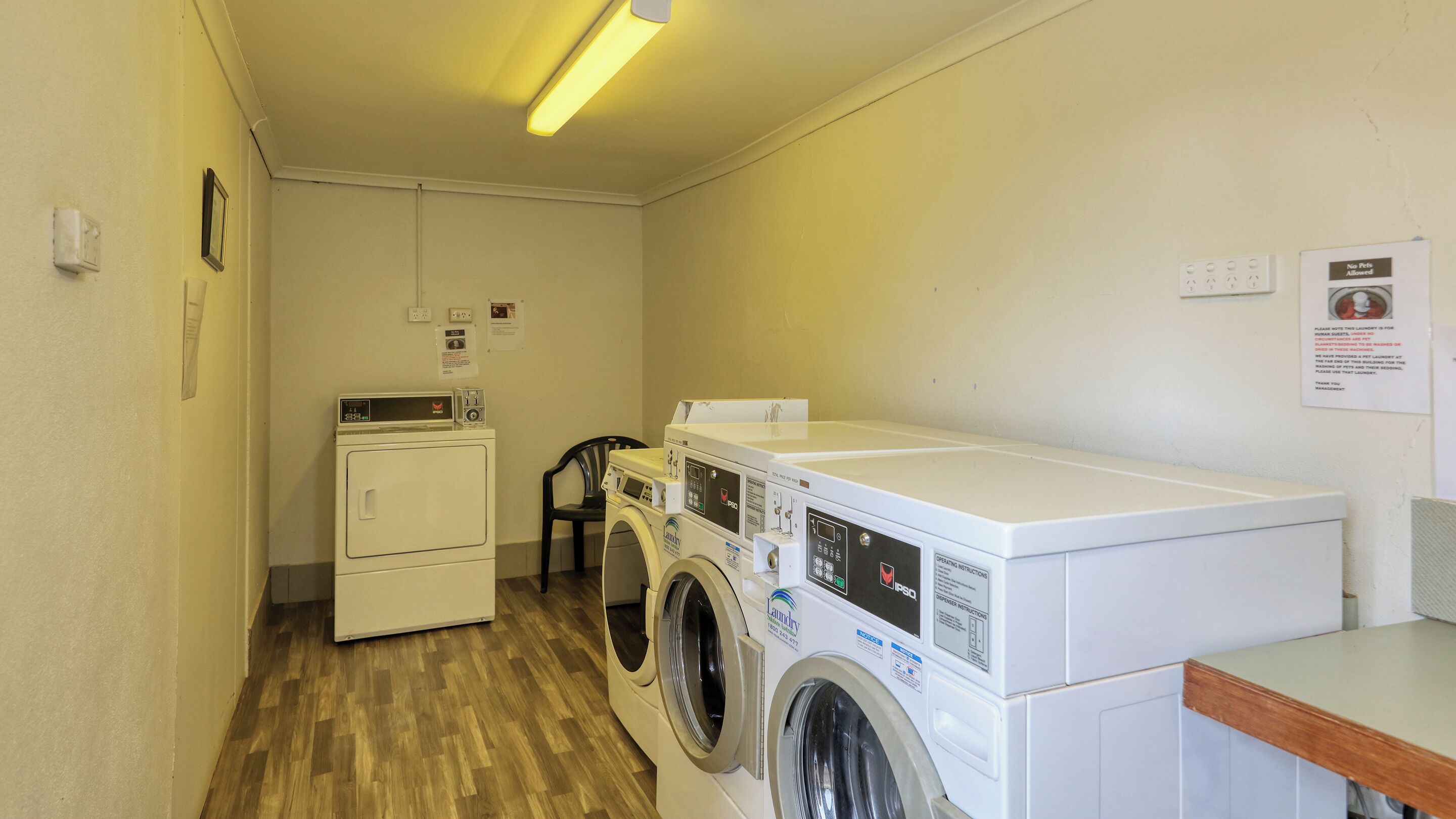 A laundry room with two washing machines, a dryer, and a chair.