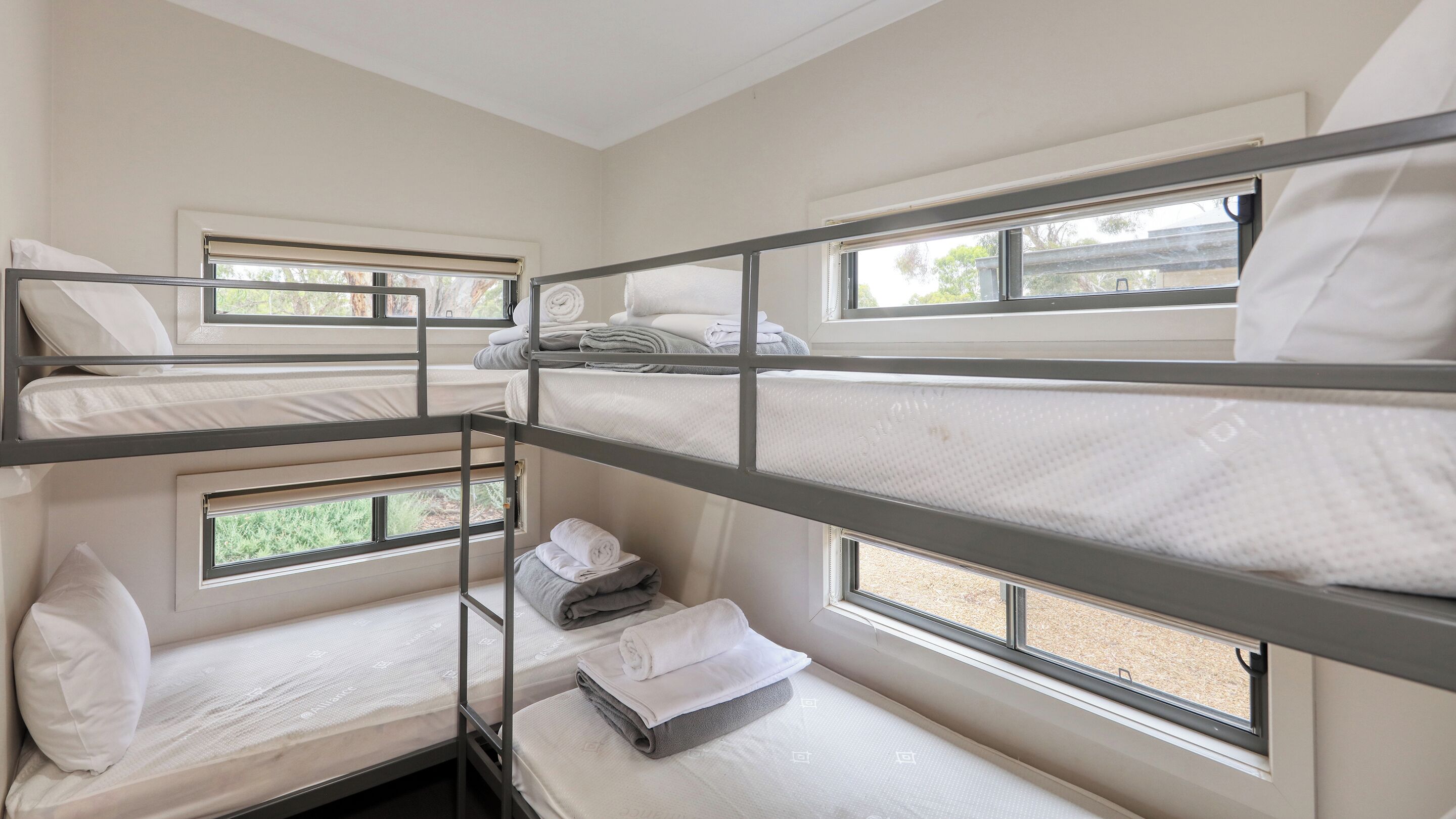 A bunk bed room with multiple beds, windows, and a view of greenery outside.