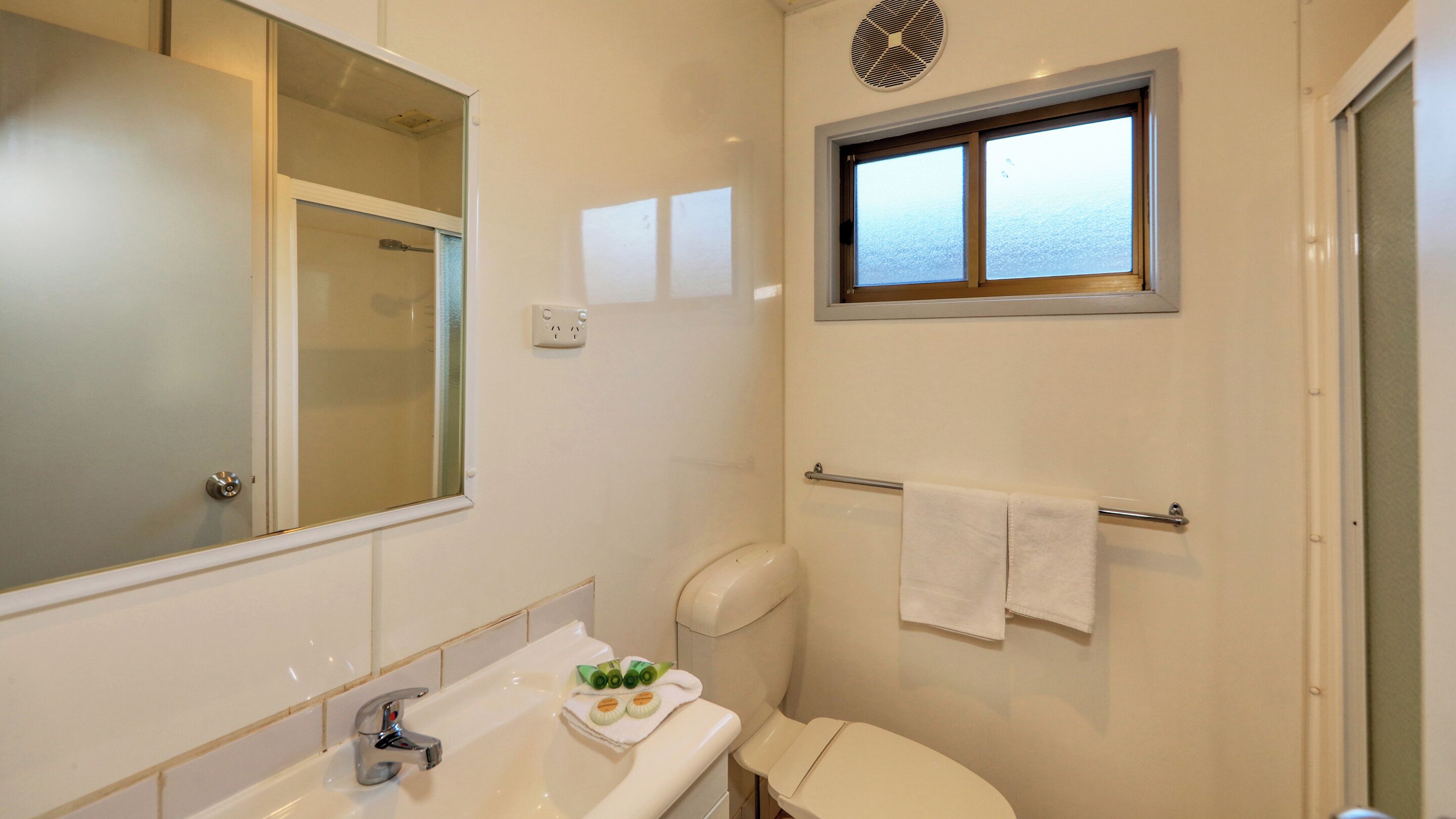 A bathroom with a large mirror, a window, a towel rack, and a toilet.