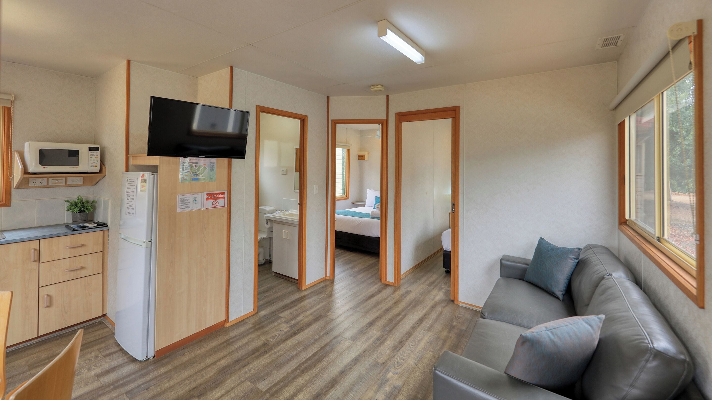 A compact room with a kitchenette, a bed, a sofa, and a television.