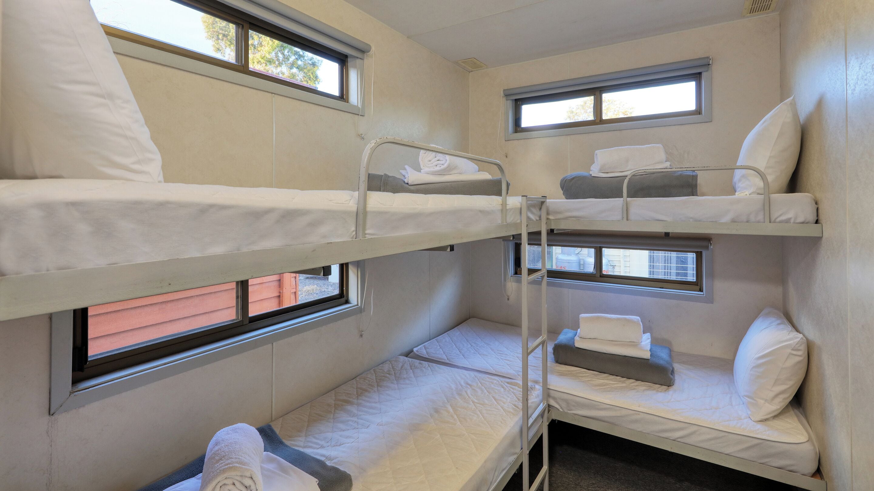 A bunk bed room with two windows, each with a view of trees. There are two beds, one on top and one below, with white bedding and pillows.