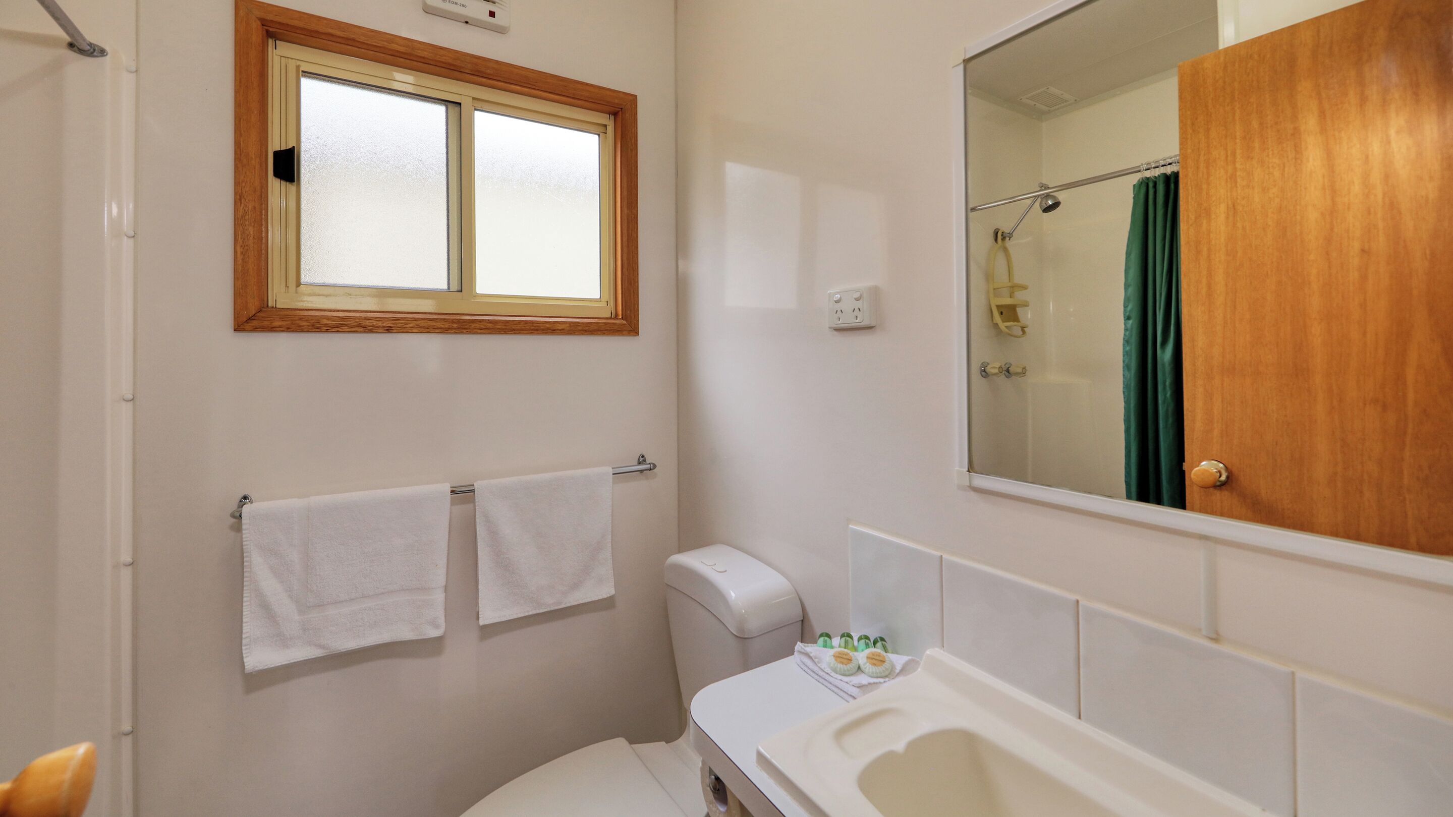Un baño con inodoro, lavamanos y bañera. Hay una ventana sobre el inodoro y un espejo sobre el lavamanos.