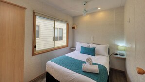 Une chambre à coucher avec un lit, une fenêtre, un ventilateur de plafond et une table de chevet avec une lampe.
