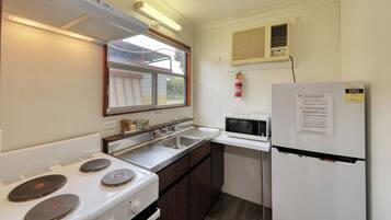 A compact kitchen with a stove, sink, microwave, and a refrigerator.