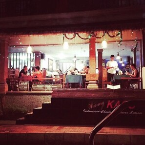 Un restaurante con terraza, una escalera que lleva a la entrada y un letrero que indica cocina indonesia.