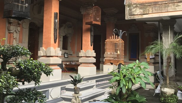 A courtyard with a traditional architectural style, featuring a central seating area with a round table and multiple stools, surrounded by potted plants and a birdcage. - Kacu guest house (Ubud)