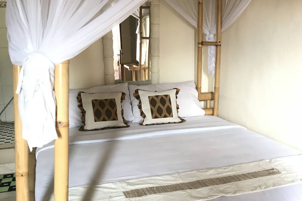 A bed with a canopy, white bedding, and patterned pillows.
