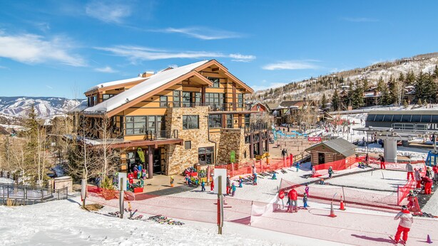 Un bâtiment d’une station de ski, avec plusieurs étages, de grandes fenêtres et, au fond, une zone où se trouve un télésiège.