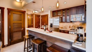 Une cuisine moderne dotée d’un îlot central, d’appareils électroménagers en acier inoxydable, de meubles de rangement en bois et de luminaires suspendus.