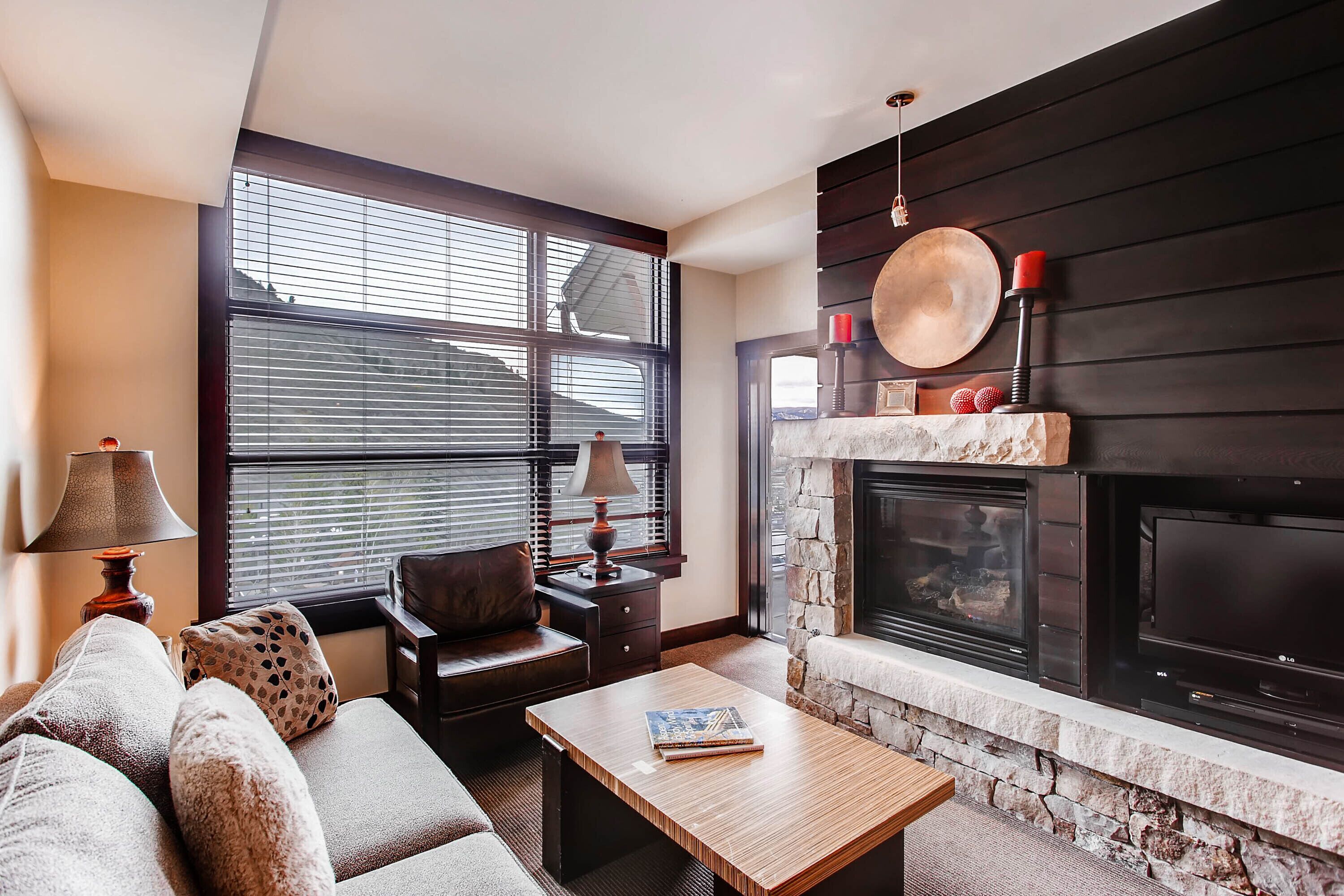 A modern living room with a stone fireplace, a sofa, a coffee table, and a TV.