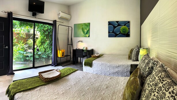 A hotel room with a bed, a desk, a chair, a TV, and a view of greenery through the sliding glass door. - Hotel Boutique Valverde Santa Elena (Antiguo Cuscatlán)