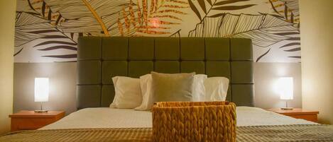 Una habitación de hotel con una cama grande, un cabecero con diseño de hojas, dos lámparas de noche y una cesta tejida sobre la cama.