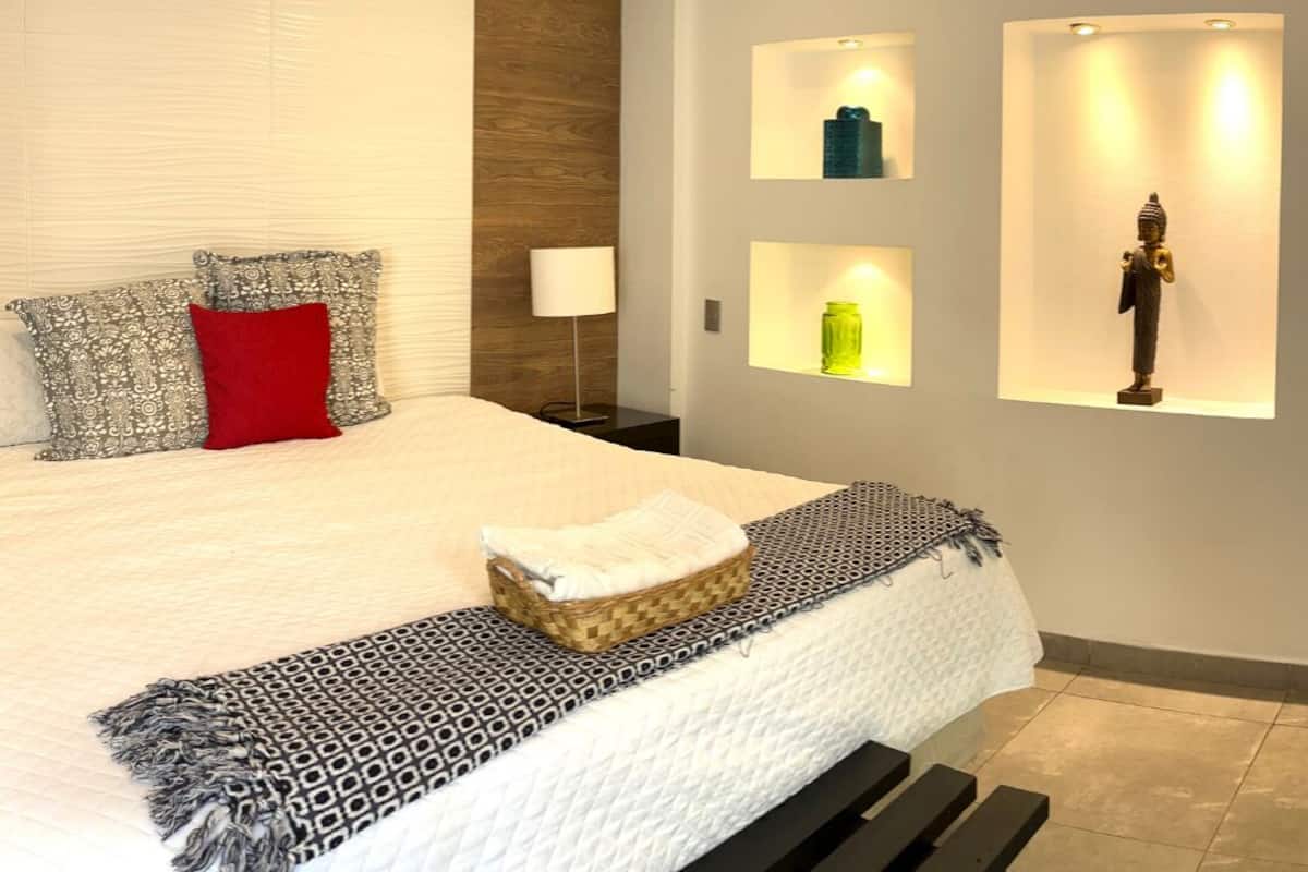 Ein modernes Schlafzimmer mit einem großen Bett, einer Nachttischlampe und Wandregalen mit Dekoration.