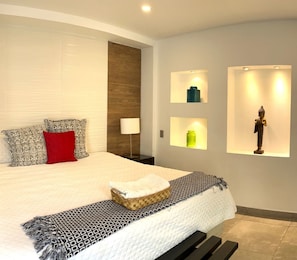 A modern bedroom with a large bed, a bedside lamp, and wall-mounted shelves with decorative items.