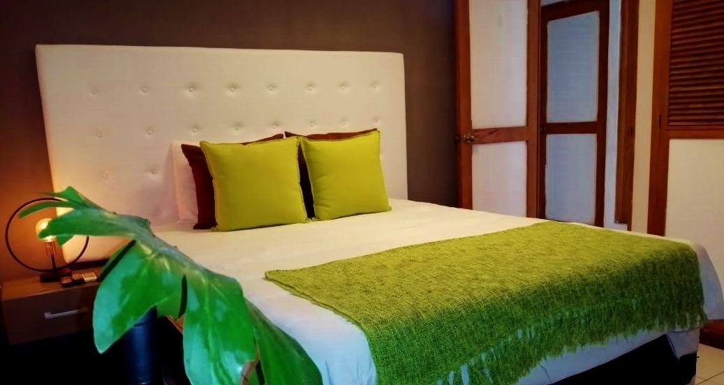 Un lit bien fait, avec une couverture verte, deux oreillers verts et une tête de lit blanche, dans une chambre d’hôtel.